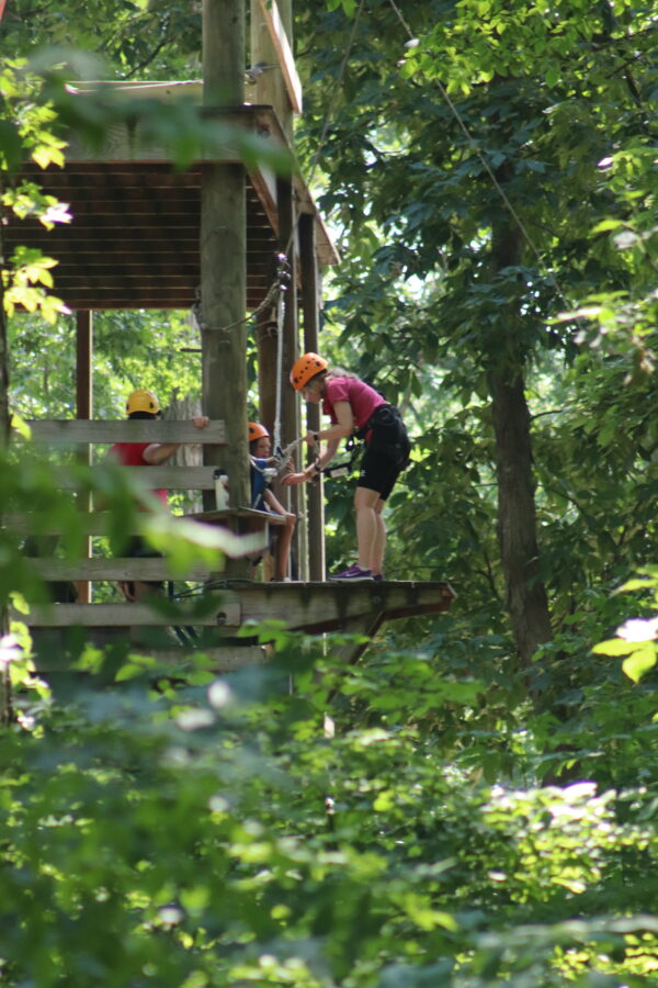A camp counselor helping a camper prepare to take on the high ropes course.