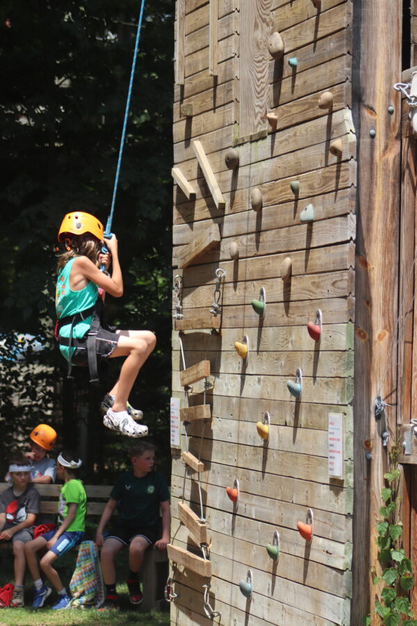 A young girl attempting to climb the rock climbing tower.