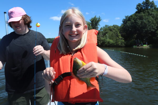 A young girl in a life jacket holding a freshly caught fish.